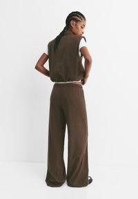 Gilet corto brown con texture a coste, abbinato a pantaloni larghi coordinati. L'outfit presenta una vestibilità morbida e un dettaglio in vita elastico.