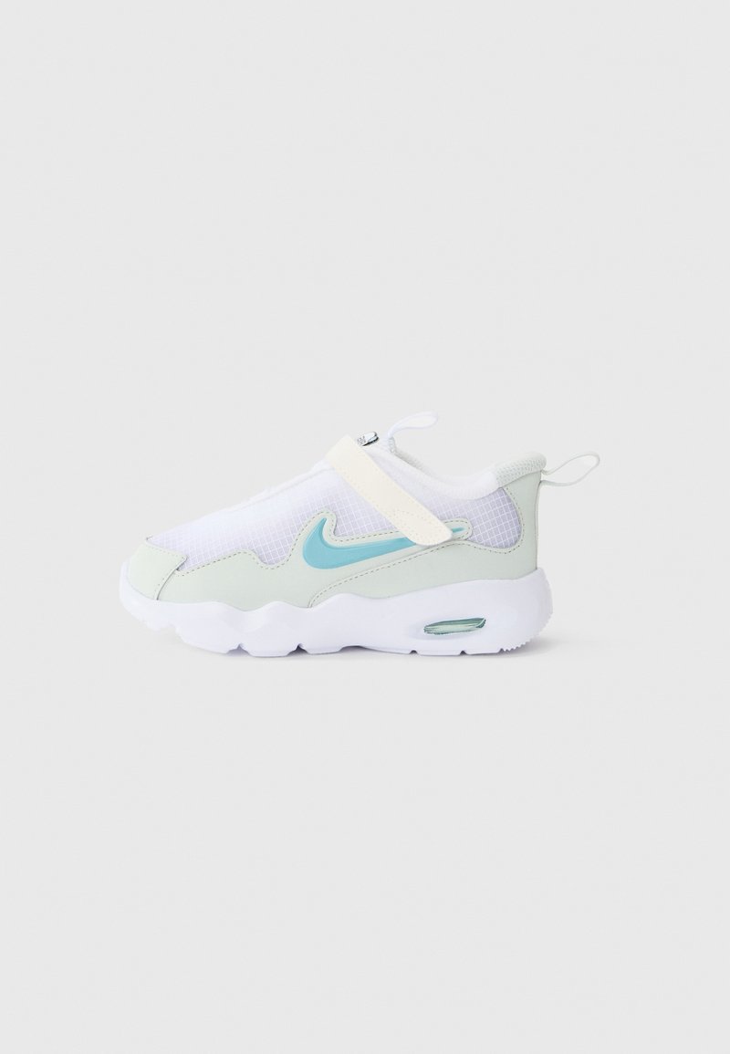 Baskets blanches et gris clair avec une virgule Nike bleue, une bande Velcro et une semelle blanche épaisse avec un coussin d'air visible, sur fond uni.