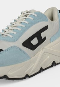 Chunky sneaker σε λευκό και ανοιχτό μπλε με λευκά κορδόνια, μαύρο λογότυπο στο πλάι και λευκή υφασμένη σόλα με μαύρες λεπτομέρειες στην πέλμα.