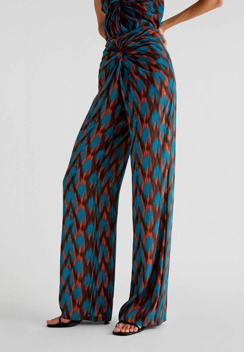 Weite Hose in einem teal-, rot- und braunfarbenen Ikat-Muster. Weicher Stoff mit einem gedrehten Knoten-Detail an der Taille, bodenlanger Schnitt.
