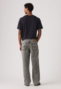 Μαύρο κοντομάνικο μπλουζάκι συνδυασμένο με χαλαρά, ξεθωριασμένα γκρι τζιν παντελόνια, με δερμάτινο πίσω ταμπελάκι και δύο πίσω τσέπες.