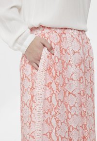 Gonna a stampa serpente rosa e bianca con elastico in vita, dotata di tasche laterali e tessuto texturizzato. Camicia bianca visibile sopra.
