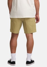 Beige cargo shorts with two side pockets, smooth fabric, and belt loops. Paired with black sneakers and white crew socks.