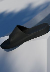 Black slide sandal with a minimalist design, smooth texture, and contoured footbed. Features a slight arch and zigzag pattern on the sole.