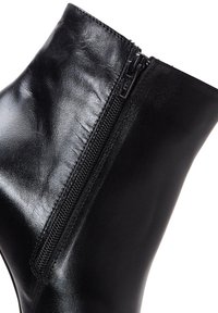 Botín negro de cuero hasta el tobillo, con una textura suave, punta redondeada y cierre con cremallera lateral. Un ligero brillo realza su aspecto refinado.