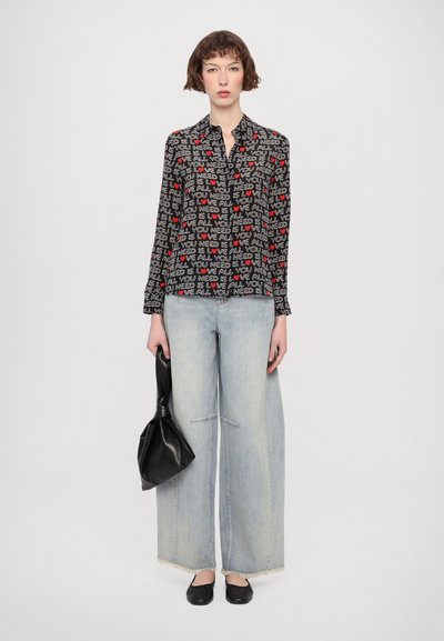 Long-sleeve shirt with a black background, red hearts, and white text. Paired with wide light blue denim, black flats, and a black handbag.