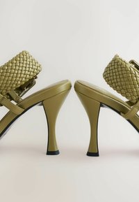 Sandale cu toc înalt de culoare verde măslin, cu curele împletite, design elegant și finisaj texturat. Tocuri notabile în formă de clepsidră.