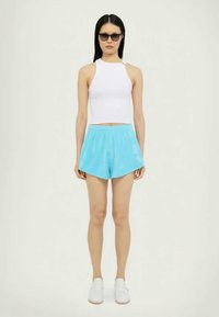 Light blue shorts made of soft fabric with a relaxed fit, paired with a white cropped tank top and white sneakers. Model wearing sunglasses.