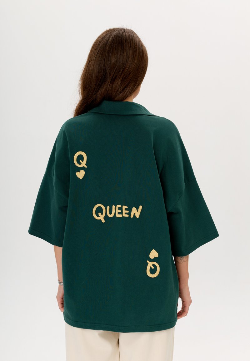 Zielona, oversize'owa koszula z krótkim rękawem, z złotym napisem "Q ♥ QUEEN" oraz symbolami na plecach, wykonana z miękkiego materiału.