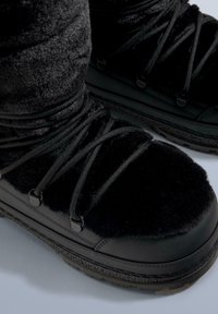 Sorte vinterstøvler med en tekstureret, fluffy overdel og en glat gummisål. Har sorte elastiske snørebånd og metaløjer for en sikker pasform.