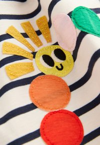 Tessuto a righe con un sole giallo ricamato e toppe circolari in arancione, rosso e verde, con dettagli facciali fantasiosi.