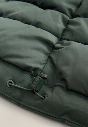 Dark green puffer jacket section featuring quilted design, smooth texture, and an adjustable drawstring with plastic hardware at the hem.
