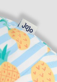Tkanina s uzorkom ananasa u žutoj i zelenoj boji na plavoj i bijeloj prugastoj pozadini, s malom oznakom "Jojo". Glatka tekstura.
