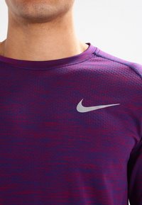 Koszulka sportowa Nike z długim rękawem w gradientowych odcieniach fioletu z teksturowanym wykończeniem. Posiada srebrne logo na lewej piersi.