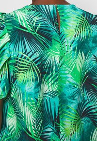 Tessuto con motivo tropicale con foglie di palma verdi e teal su uno sfondo blu, con chiusura a forma di chiave sulla schiena e dettagli con maniche arricciate.