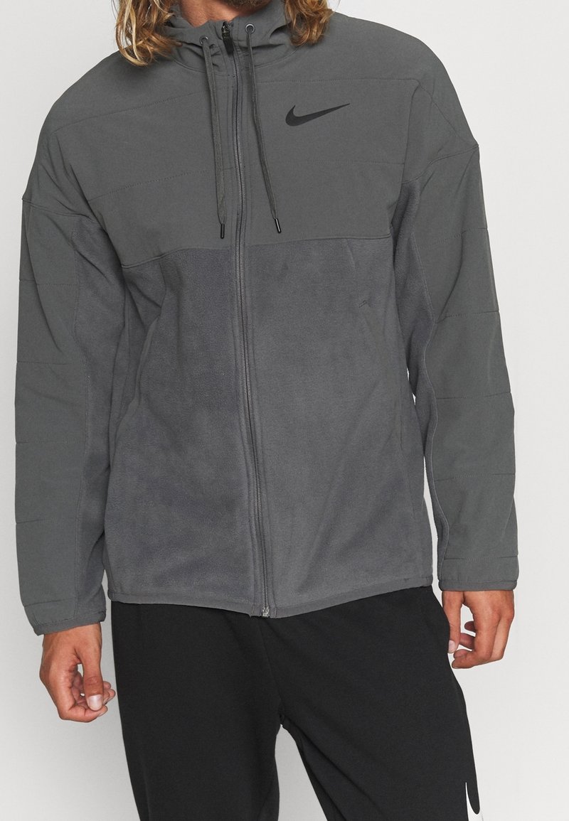 Giacca zip-up Nike grigia con cappuccio, caratterizzata da una texture liscia, pannelli in contrasto chiaro e scuro e logo frontale in nero.