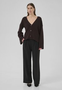 Cardigan oversized marron foncé avec un col en V, cinq boutons, ourlet côtelé et manches larges, assorti à un pantalon noir taille haute et des chaussures noires à talons pointus.