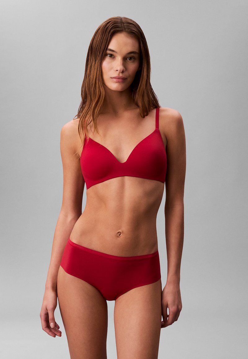 Bralette rojo sin costuras con tirantes delgados ajustables y diseño de escote en V, acompañado de bragas tipo hipster rojas a juego, textura de tela suave.