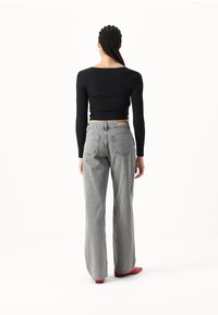 Top negro de manga larga acanalado combinado con unos vaqueros grises de talle alto y corte holgado, y zapatos rojos. Diseño simple y funcional con acentos mínimos.