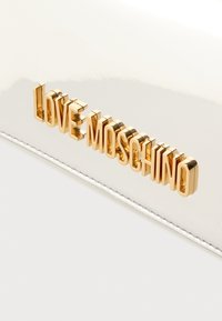 Λευκή τσάντα από δέρμα με πατίνα, με ανάγλυφη χρυσή επιγραφή "LOVE MOSCHINO". Λεία υφή με γυαλιστερό φινίρισμα και ασημένιες διακοσμητικές ραφές.