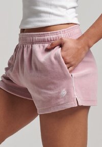 Pantalones cortos de algodón rosa con cintura elástica, bolsillos laterales y un pequeño logo bordado en la parte delantera. Presentan un acabado suave y texturizado.