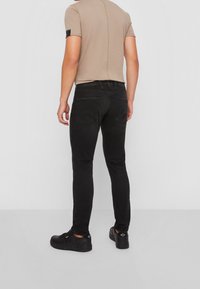 Mörk denimjeans med slim fit; har en klassisk femfickedesign och kontrasterande sömmar. Bärs med en ljusbeige kortärmad skjorta.