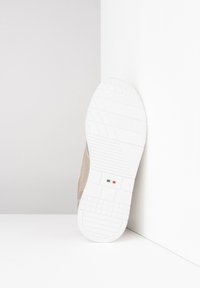 Beige sneaker with a textured upper, white rubber sole, and a small green-white-red Italian flag detail on the sole.