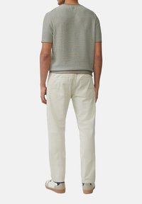 Lichtgrijs gebreid shirt met textuur, witte broek en lichte sneakers met donkere accenten. Heeft een casual pasvorm en een opvallend ontwerp van de achterzak.