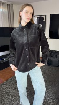 Juoda kordurovinė marškiniai su sagomis, kišene, laisvo kirpimo, ilgomis rankovėmis ir tekstūruota medžiaga, derinama su šviesiai mėlynais tiesaus kirpimo džinsais.