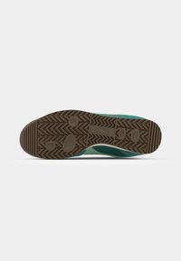 Groene sportieve schoenzool van textuurrubber, met zigzagpatronen en ronde grip. Degelijke bruine sectie nabij de teen voor duurzaamheid.