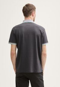 Polo de color gris oscuro con un cuello y acentos de manga de rayas en azul claro que contrastan. Fabricado con un tejido suave y con un corte relajado.