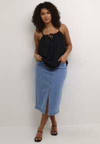 Top nero senza maniche con una cintura frontale, abbinato a una gonna midi in denim blu chiaro con spacco anteriore e design aderente, completato da sandali neri.