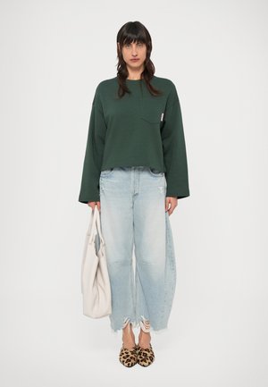 Sweat-shirt vert court à manches longues, jean à jambes larges bleu clair avec ourlet effiloché, chaussures à imprimé léopard et sac fourre-tout blanc.