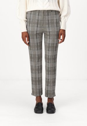 Graue Karottenhose mit schmalem Schnitt und verkürzter Länge, die eine Mischung aus kräftigen und dezenten Streifen aufweist, kombiniert mit schwarzen Slippers.