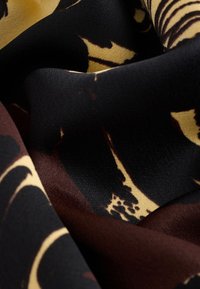 Tessuto setoso con base nera, caratterizzato da un motivo floreale astratto giallo e marrone. La texture appare liscia e leggermente lucida.