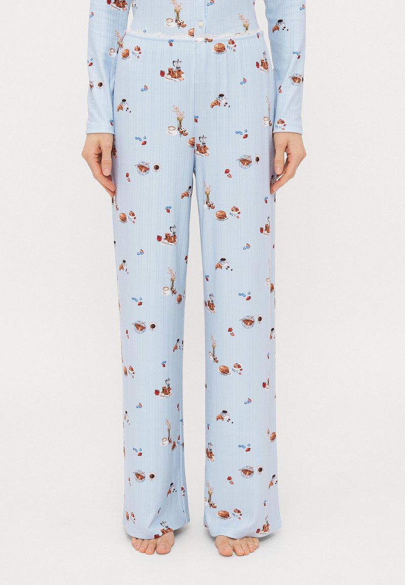 Lyseblå pyjamas sættet med ribbet tekstur, der har et mønster af desserter og drikkevarer. Lange, løst siddende bukser med snor i taljen.