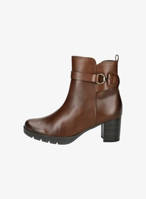 Botín de cuero marrón hasta el tobillo con punta redondeada, correa lateral, decoración metálica y un tacón grueso; suela de goma texturizada para mayor agarre.