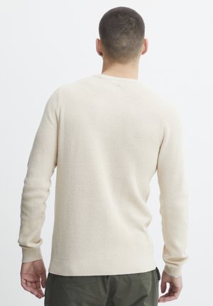 Light beige knitted sweater with a ribbed texture, round neckline, and long sleeves, featuring a straight hem and minimalistic design.