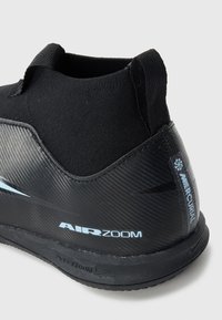 Gros plan sur le talon d'une chaussure de football Nike Air Zoom Mercurial noire avec un logo bleu clair et un matériau synthétique texturé.