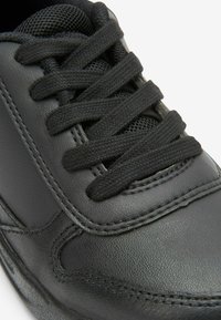 Sneaker in pelle nera con lacci neri piatti, superficie texturizzata e cuciture a contrasto. Presenta una punta arrotondata e una caviglia imbottita.