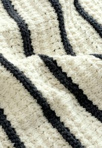 Plaid di lana lavorato a maglia con strisce alternate di crema e grigio scuro. Il materiale appare morbido con un motivo strato accogliente.