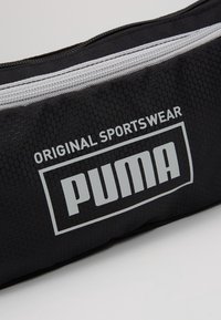 Svart sportväska med en strukturerad hexagonal mönster, med en vit dragkedja och "PUMA"-logotyp i fet, vita bokstäver.