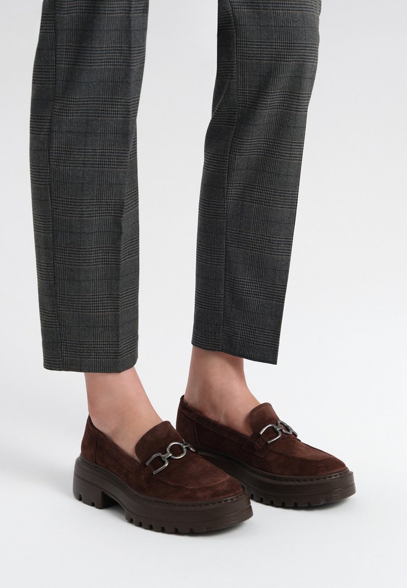 Loafers din suede maro cu o talpă groasă, având un accent din lanț metalic argintiu în partea din față și un finisaj texturat.