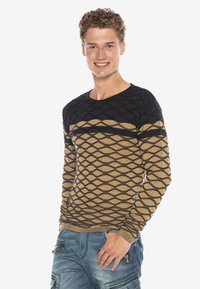 Beiger Pullover mit schwarzem Rautenmustern und gestreiftem Design, strukturiertem Stoff, Rundhalsausschnitt, getragen mit hellblauen Cargo-Hosen.