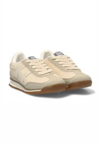 Zapatillas beige con parte superior de tela texturizada, dos franjas en los laterales, puntera redonda y suela de goma con una suela exterior marrón contrastante.