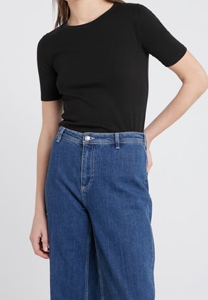 T-shirt noir à manches courtes associé à un jean en denim bleu taille haute, présentant une coupe classique et des détails de couture légers.