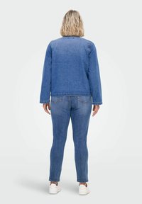 Jeans jakna in prilegajoče hlače v srednje modri barvi. Jakna ima dolge rokave in raven kroj; hlače so ožane z minimalnimi detajli šivanja.