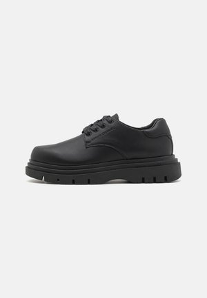 Scarpe stringate in pelle nera con una suola in gomma spessa e texturizzata. Design semplice senza modelli visibili e con un marchio discreto sul lato.