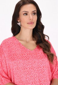 Top cu guler în V de un roz strălucitor, cu un model de leopard. Prezintă mâneci largi și o textură de țesătură ușoară. Cerceii strălucitori pun în valoare look-ul.