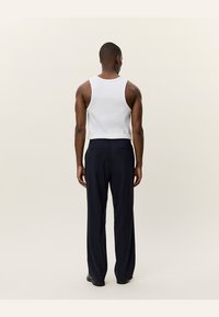 Hvit tank topp og marineblå bukser, tettsittende i midjen, med en glatt tekstur og rett snitt. Enkelt design, ingen fremtredende mønstre eller detaljer.